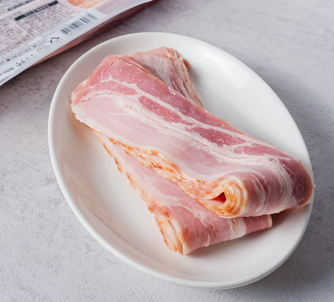 차별화상회 크레잇 맛있는 베이컨 냉동 패키지와 화이트 타원형 접시에 신선하게 겹쳐진 베이컨 슬라이스 연출 메인 이미지