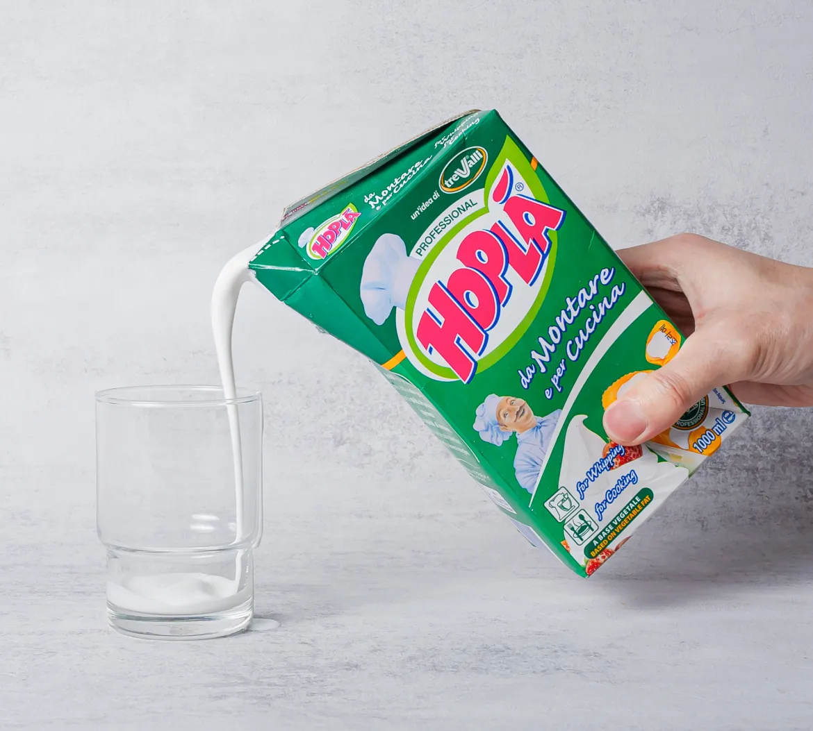 홉라 식물성 휘핑크림 500ml 팩을 가볍게 쥐고 유리잔에 흰 크림 액상을 따르는 연출 이미지